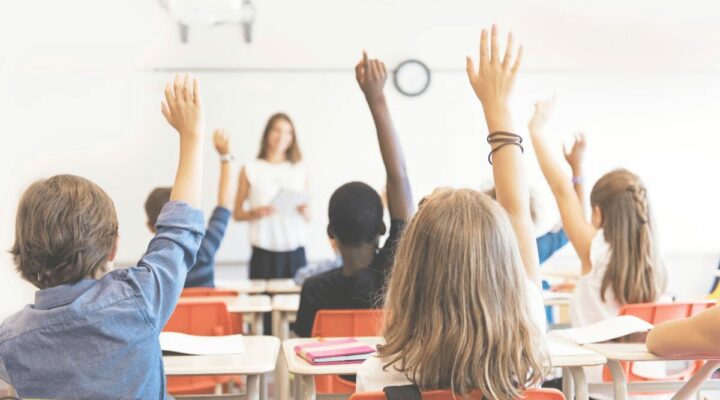 A classroom with students raised to participate in classroom discussion